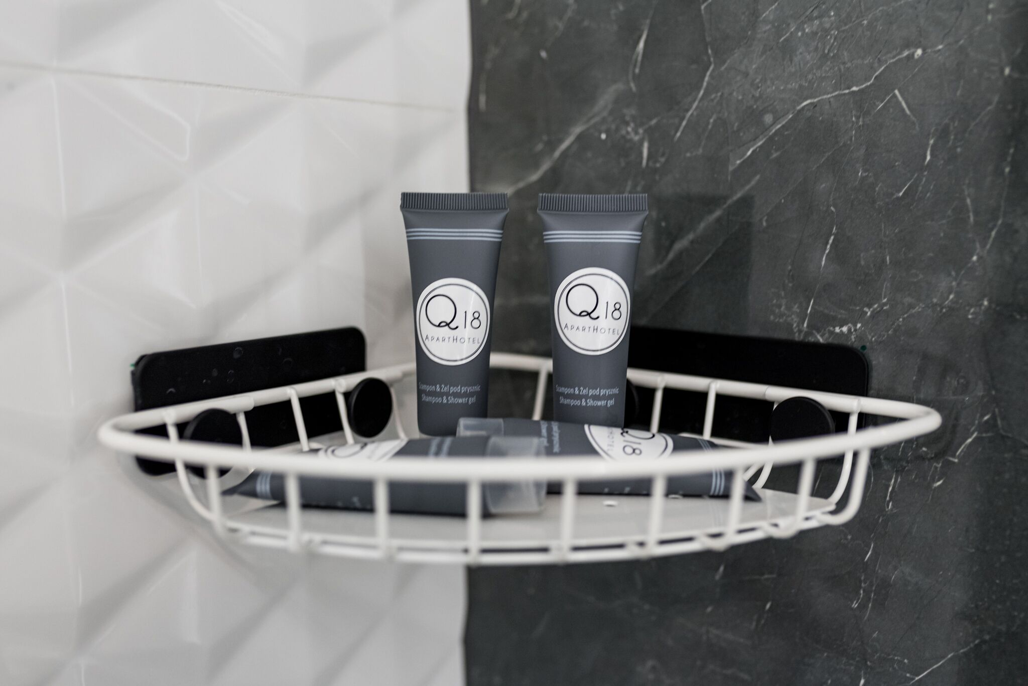 Two toiletry tubes labeled 'Q18' on a white shelf against a marble wall.
