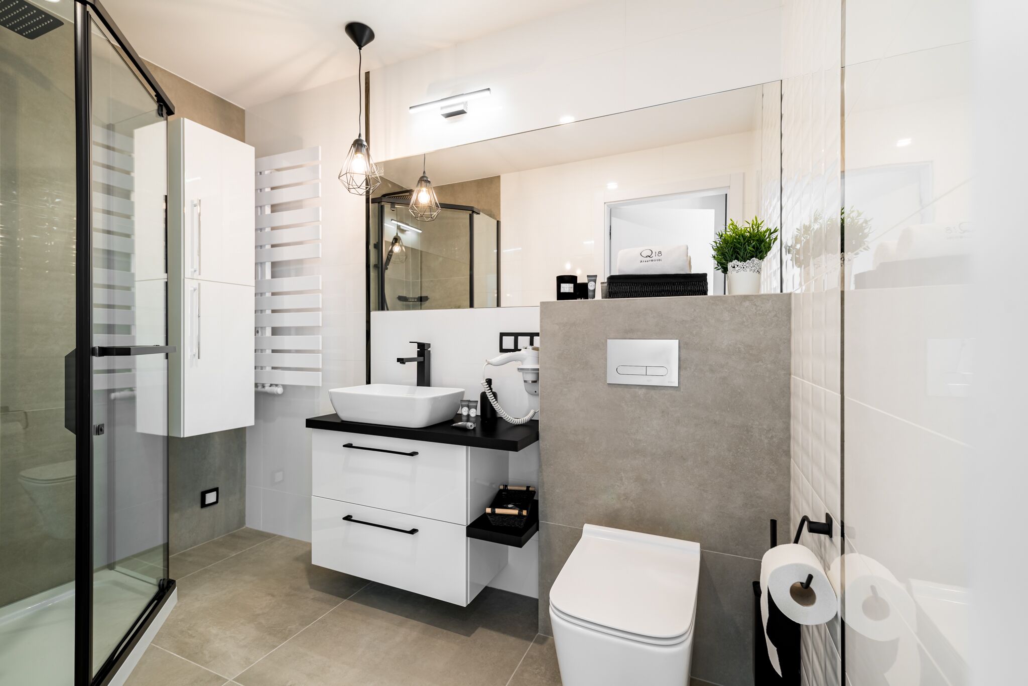 A modern bathroom with a glass shower enclosure, a white sink, a black countertop, and a white toilet.