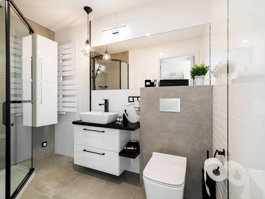 A modern bathroom with a glass shower enclosure, a white sink, a black countertop, and a white toilet.