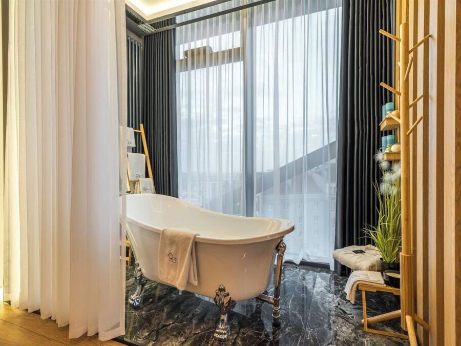 Un baño moderno con una bañera independiente, suelo de mármol y vistas a la ciudad a través de amplias ventanas.