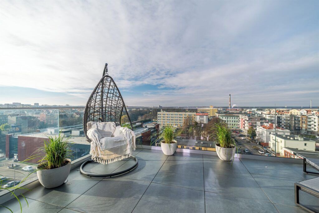 A rooftop terrace with a hanging chair, potted plants, and a city view.