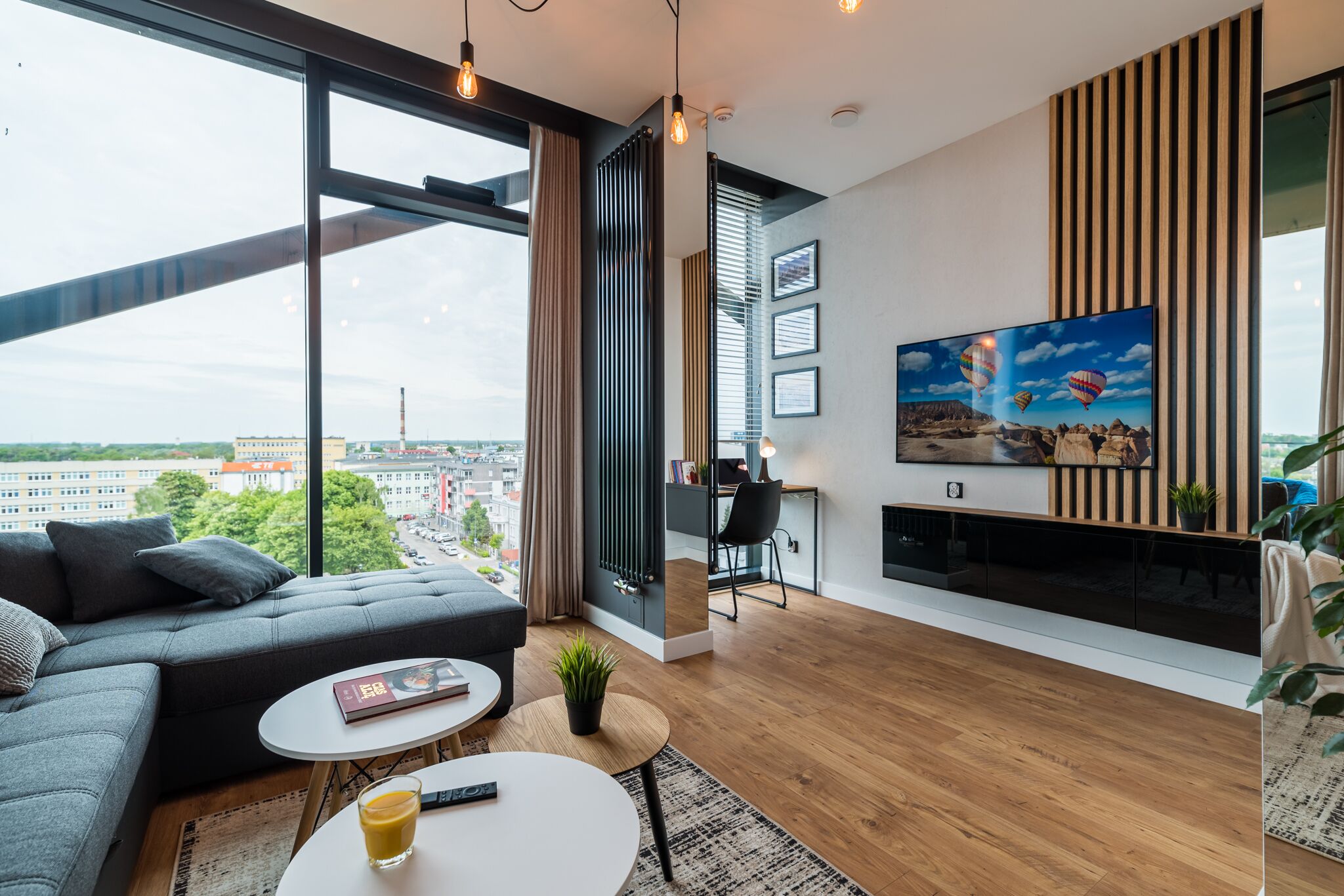 A modern living room with a large window, a sofa, a coffee table, and a TV mounted on the wall.