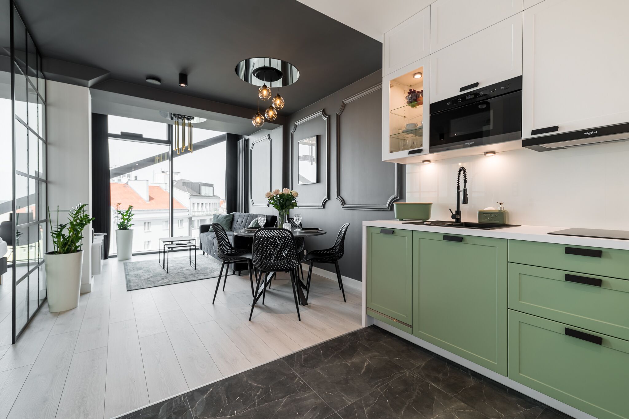 A modern kitchen with green cabinets, a black microwave, and a dining area with a table and chairs.