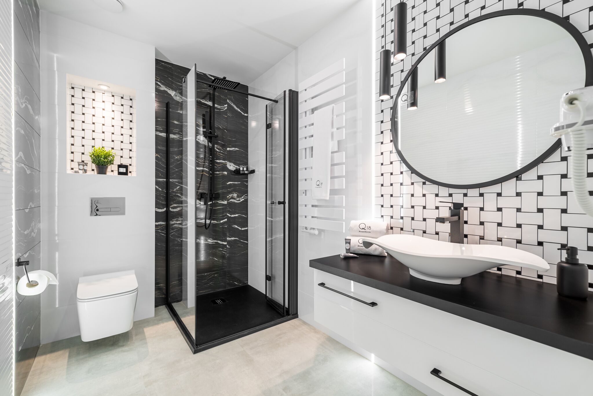 Un baño moderno con ducha envuelta en vidrio, inodoro blanco, lavamanos de mármol negro y un espejo grande.