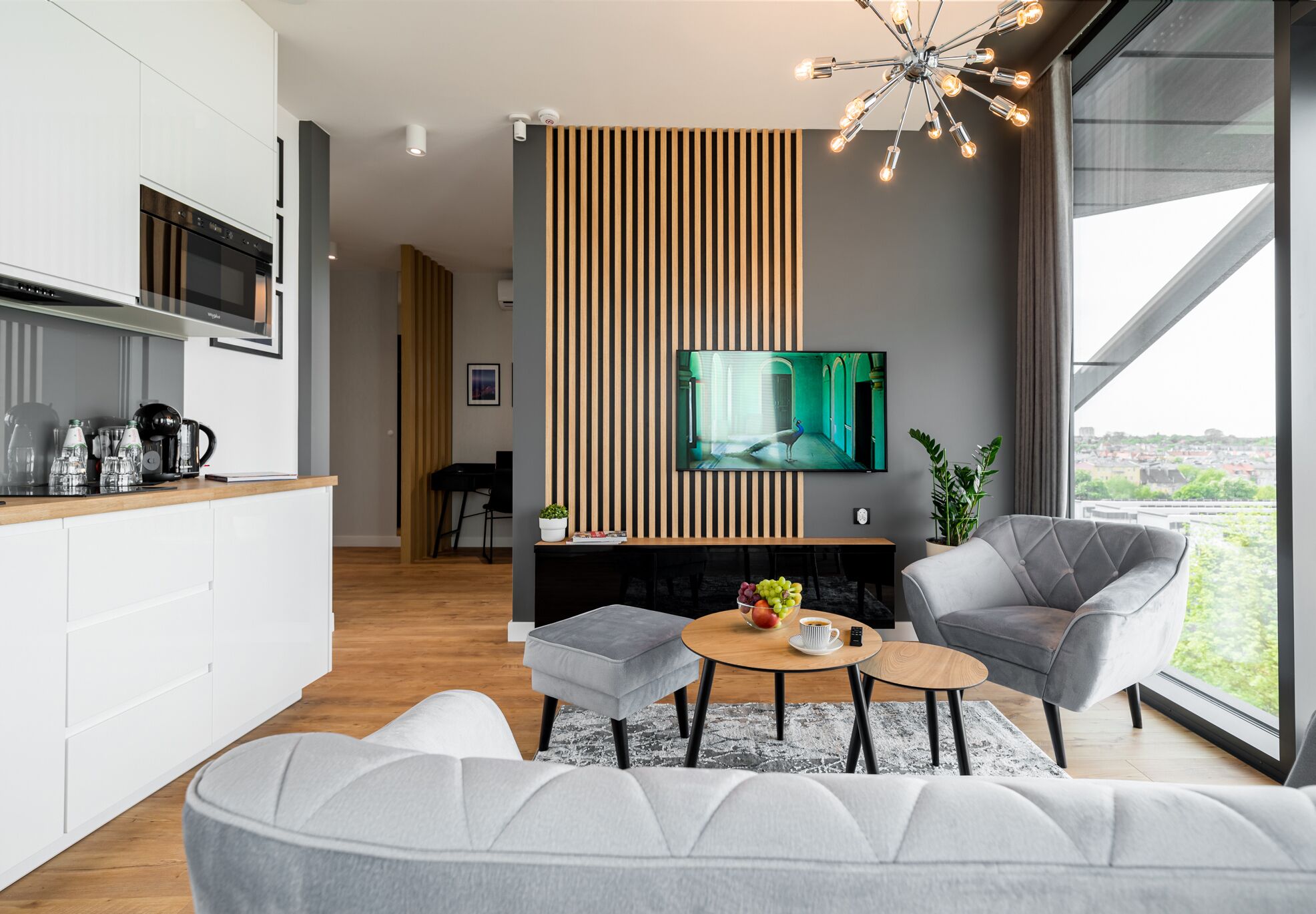 A modern living room with a grey sofa, a coffee table, and a TV mounted on a wall with vertical wooden slats.