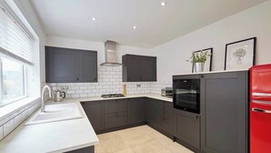 Una cucina moderna con mobili scuri, un piano di lavoro bianco, un frigorifero rosso e una finestra che lascia entrare luce naturale.