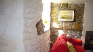 A room with a stone wall, a red sofa with a yellow pillow, and a framed picture on the wall.