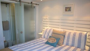 A bedroom with a bed, striped bedding, a bedside table, a nightstand, a lamp, a picture on the wall, and a sliding door closet.