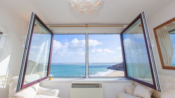 A room with a large bay window overlooking a beach, a white radiator, and a modern light fixture. - 13 Carrack Widden - amazing sea views with spa passes (St Ives)