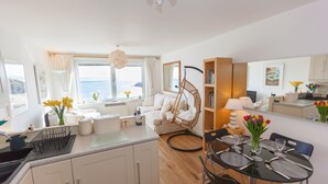 A modern kitchen with white cabinets, a dining area with a glass table, and a view of the sea. - 13 Carrack Widden - amazing sea views with spa passes (St Ives)