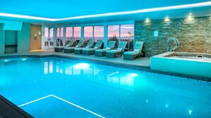 An indoor swimming pool with lounge chairs, a stone wall, and a view of the sunset. - 13 Carrack Widden - amazing sea views with spa passes (St Ives)