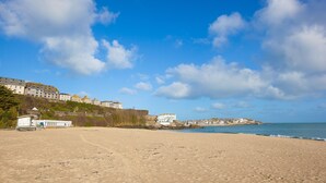 A beach with a lifeguard tower, buildings along the shore, and a clear blue sky. - 13 Carrack Widden - amazing sea views with spa passes (St Ives)
