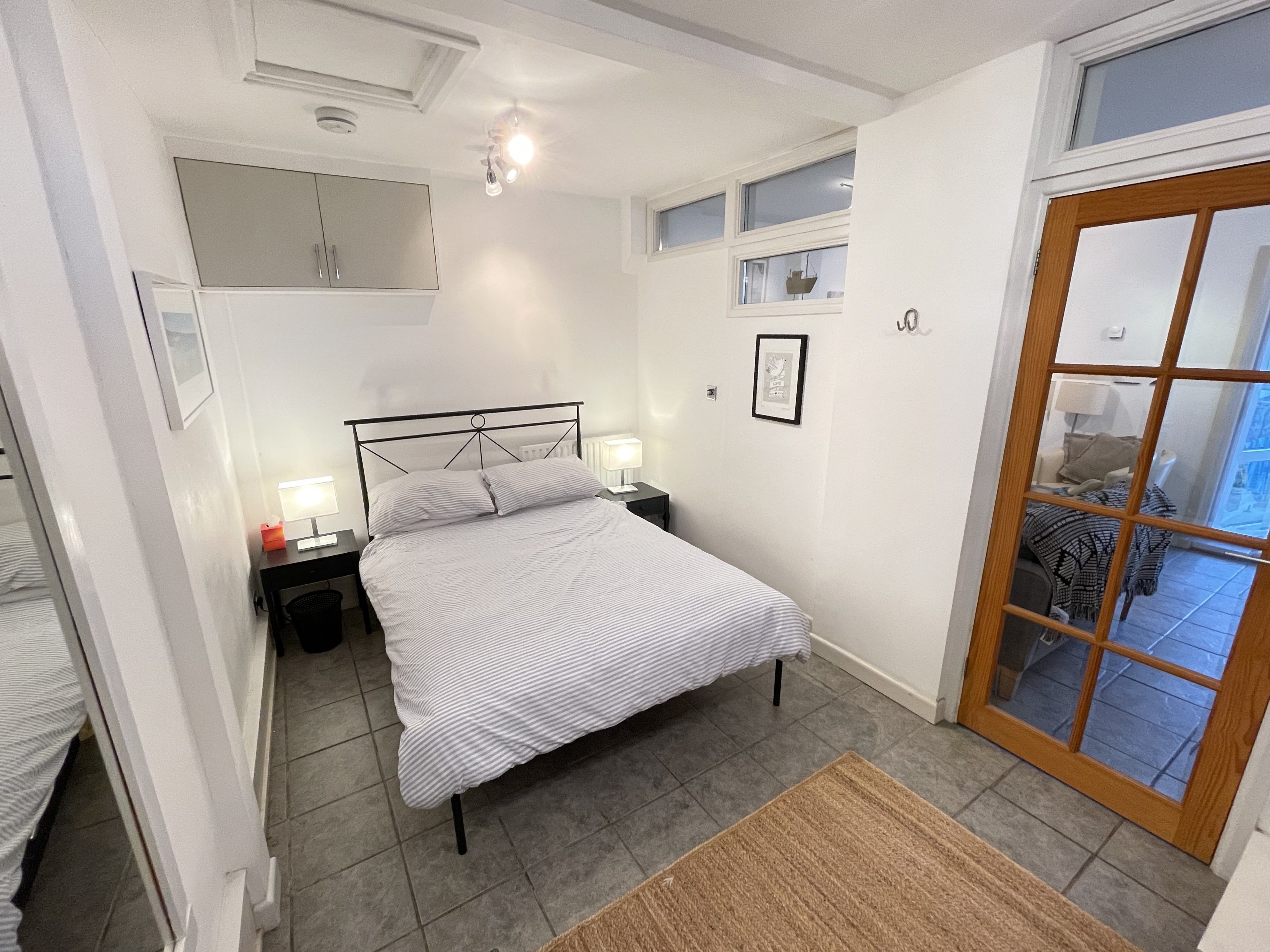 Un dormitorio con cama, mesitas de noche, una ventana y una puerta.