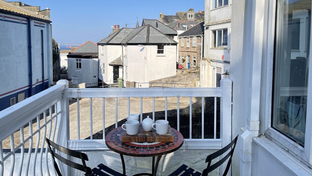 Un balcón con una mesa preparada para el té, con vistas a una calle con edificios tradicionales.