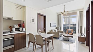 Een modern appartement met keuken, eethoek en woonkamer. Het heeft een eettafel, stoelen, een bank en een balkon met uitzicht op de stad.