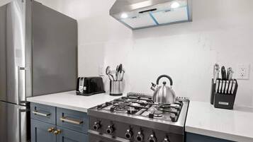A kitchen with a stainless steel refrigerator, a gas stove, a toaster, and a kettle.