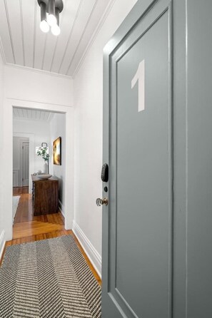 A hallway with a gray door marked with the number 1, a wooden floor, and a patterned rug.