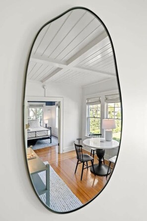 A room with a round table and chairs, a bed with a white headboard, and a window with a view of greenery.