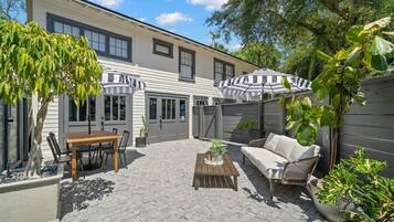 A patio with a table and chairs, a sofa, and two striped umbrellas.