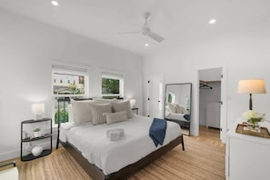A modern bedroom with a large bed, bedside tables, a ceiling fan, and a view of the outside.