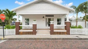 A white colonial-style house with a front porch, brick columns, and a white picket fence.