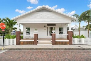 A white colonial-style house with a front porch, brick columns, and a white picket fence. - Otis Blue at Angels Quarter | Home Steps to 7th! (Tampa)