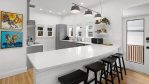 A modern kitchen with white cabinetry, a large island with bar stools, pendant lighting, and artwork on the walls.