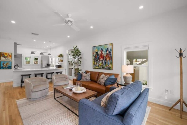 A modern living room with a sofa, coffee table, and chairs, a kitchen area with bar stools, and a dining table.