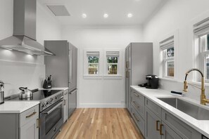 Une cuisine moderne avec des meubles blancs, une hotte en acier inoxydable, un four encastré et une grande fenêtre donnant sur un paysage verdoyant.
