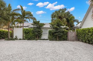 Uma área residencial com um caminho de acesso de cascalho, palmeiras e uma casa com fachada branca.