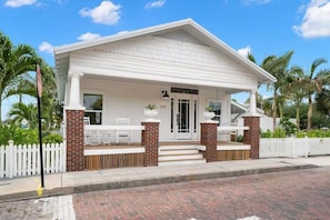 A white building with a porch, brick columns, and a white picket fence.