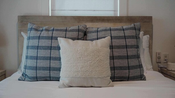 A bed with a headboard, two patterned pillows, and a fluffy pillow.