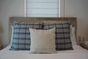 A bed with a headboard, two patterned pillows, and a fluffy pillow.