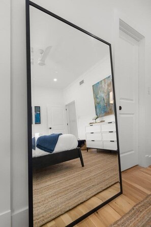 Een slaapkamer met een bed, een witte dressoir, een schilderij en een grote spiegel.