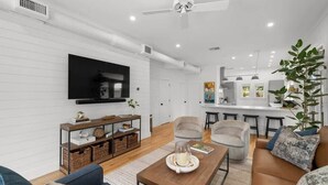 A modern living room with a TV, sofas, a coffee table, and a kitchen area in the background.