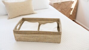 A neatly made bed with a woven basket in front, a bedside table with a lamp, and a wooden dresser.