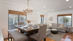 A modern dining area with a wooden table, upholstered chairs, and a chandelier.