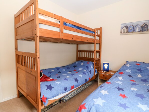 A bunk bed room with a star-patterned bedspread, a nightstand with a book and a lamp, and a painting on the wall.