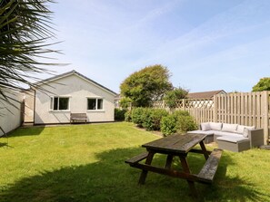 A backyard with a house, a wooden fence, a picnic table, and a wicker sofa.