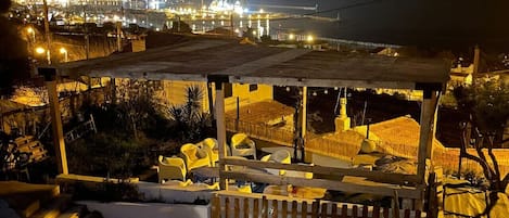 Tagterrasse med udendørs siddepladser, udsigt over bybilledet om natten og et vandareal i baggrunden.
