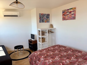 Une chambre à coucher comprenant un lit, un bureau, une chaise, un téléviseur, une armoire et des œuvres d’art murales.