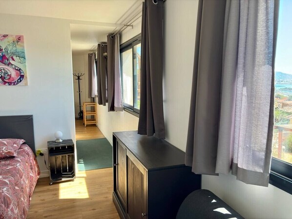 A bedroom with a bed, a dresser, a coat rack, and a window with curtains.