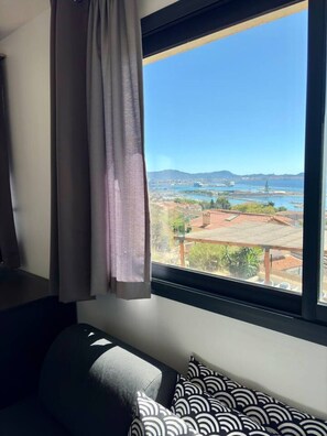Una habitación con un ventanal grande, una cama con almohadones estampados y vistas a un paisaje costero.
