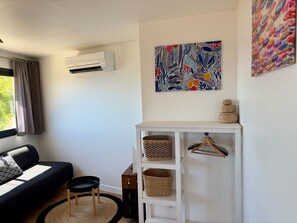 A room with a black sofa, a white cabinet with baskets, a hanging artwork, and an air conditioning unit.