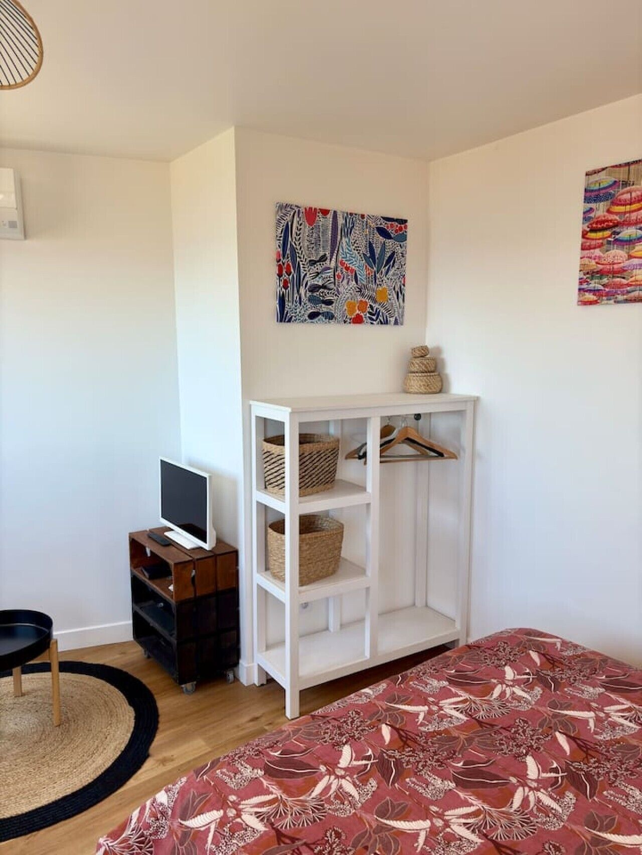 A bedroom with a bed, a TV on a wooden stand, a white wardrobe, and two abstract paintings on the walls.