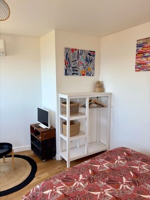 A bedroom with a bed, a TV on a wooden stand, a white wardrobe, and two abstract paintings on the walls.