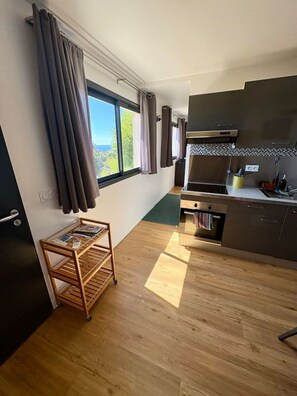 A modern kitchen with a wooden floor, a built-in oven, and a window with curtains.