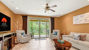 Ein Wohnzimmer mit Fernseher, zwei Sesseln, einer Couch, einem Couchtisch und einem Deckenventilator.
