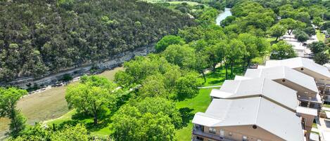 A residential area with a river, lush greenery, and a multi-story building with balconies.