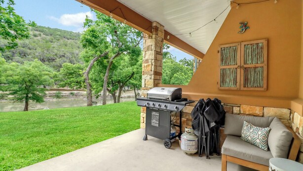 Eine überdachte Terrasse mit Grill, einer Couch und Blick auf eine grüne Landschaft.